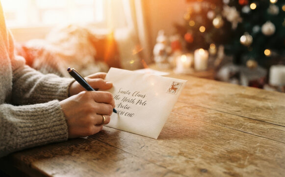 Woman writing a letter to Santa Claus for Christmas on a wooden table at home with festive tree in the background