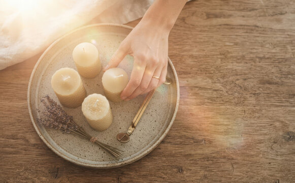 Woman arranging handmade beeswax candles with lavender on a ceramic tray for relaxation and home decor