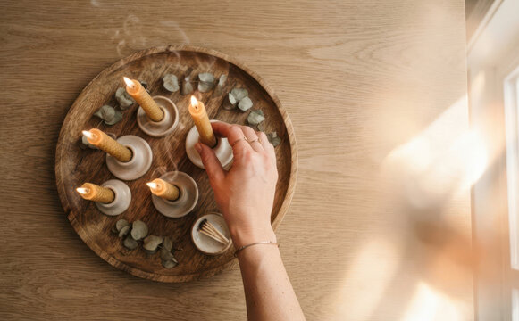 Woman lighting beeswax candles in holders on a wooden tray for relaxation and cozy atmosphere at home