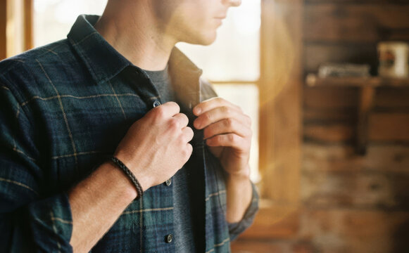 Young adult man wearing a plaid flannel shirt buttoning up indoor lifestyle portrait concept