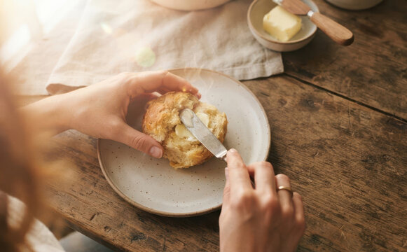 Woman spreading fresh butter on warm bread roll at wooden table for breakfast, rustic home cooking and comfort food lifestyle concept