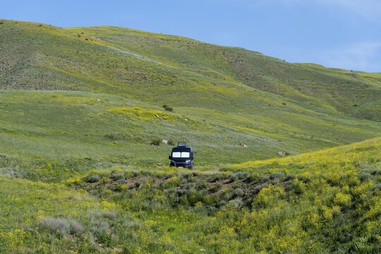 A black van stands alone in a meadow next to green and yellow hills under a blue sky, camper, landscape near Hatsavan, Kotayk province, Kotayk, Armenia