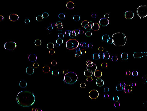 Soap Bubbles floating over black background isolated. Rainbow colorful air balls fly over many sizes. Shampoo bubbles sphere form shiny glossy blowing transparent purity in group.