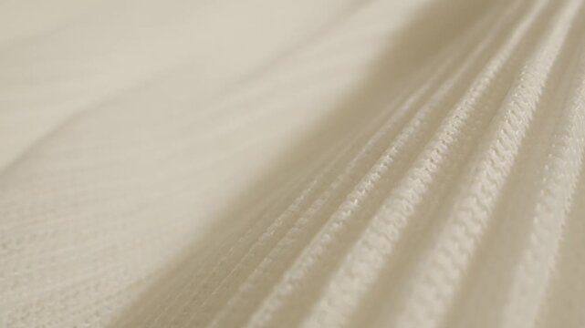 Ribbed fabric texture in cream color, close up of soft pleated knit textile with hand touching, beige knitted cloth background for fashion design and interior upholstery