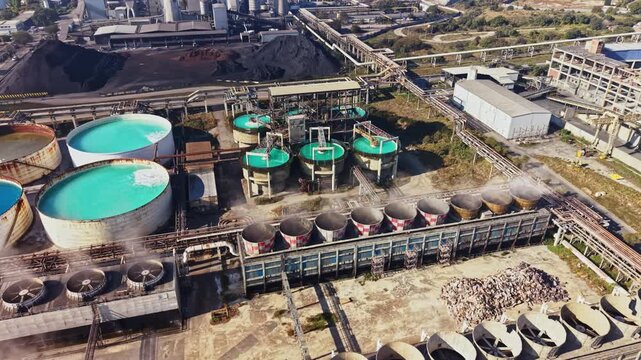 Water tanks and processing equipment stand among pipe networks at an industrial plant, viewed from above in daylight.