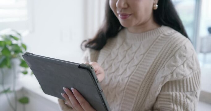 Woman holding tablet case, navigating app, tapping and swiping, wearing watch in kitchen