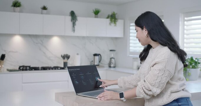 Woman seeing open laptop at kitchen island leaning and tapping shopping-list on screen, copy space