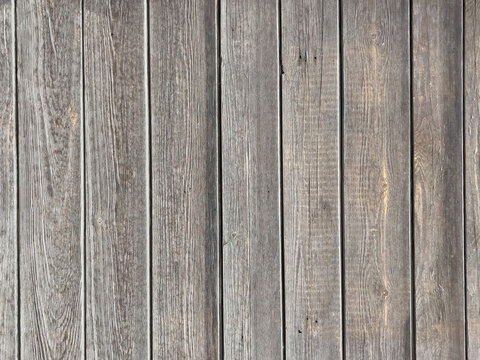 Weathered wooden plank panel with vertical grain texture and aged gray brown patina, close-up detail for background and surface use, rustic flooring or siding material sample