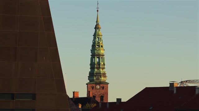 Aerial drone view of a green copper church spire with a clock beside the dark wall of the Black Diamond, Copenhagen, Denmark.