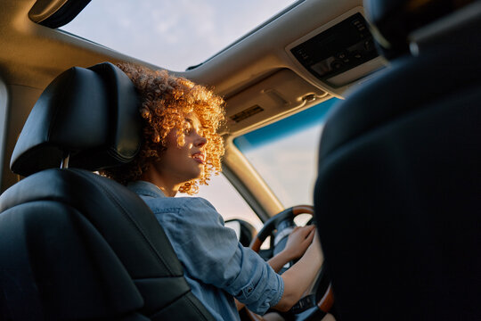 Woman driving car interior casual lifestyle portrait with sunlight on hair, focused on road, conveying relaxed mood and authentic everyday travel in a vehicle