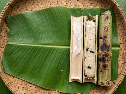 Thai khao lam sticky rice roasted in bamboo, split open on banana leaf and woven tray, traditional Thai snack, top view