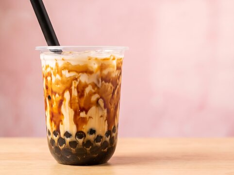 Brown sugar boba milk tea with tapioca pearls and syrup swirls in plastic cup on pink background