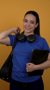 Beautiful latina college student with a backpack, tablet, and headphones smiling at the camera