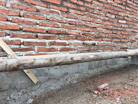 Unfinished red brick wall with horizontal wooden beam and concrete foundation on active construction site, ideal for civil engineering, masonry building, and house structure stock photo.