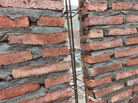 Unfinished red brick wall under construction with an exposed vertical steel rebar column frame in between, ideal for building development, architecture masonry, and house structural photo.