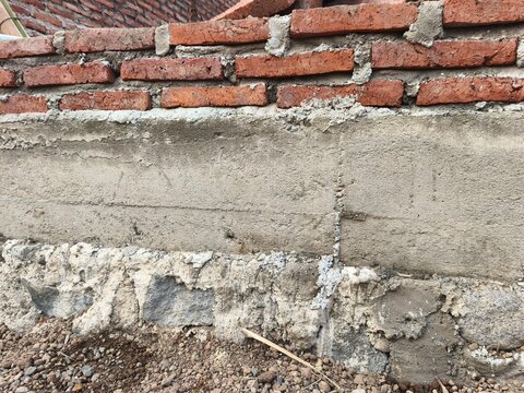 Close up view of building foundation with stone masonry, concrete tie beam, and unfinished red brick wall on construction site, ideal for house structure material and civil engineering photo.