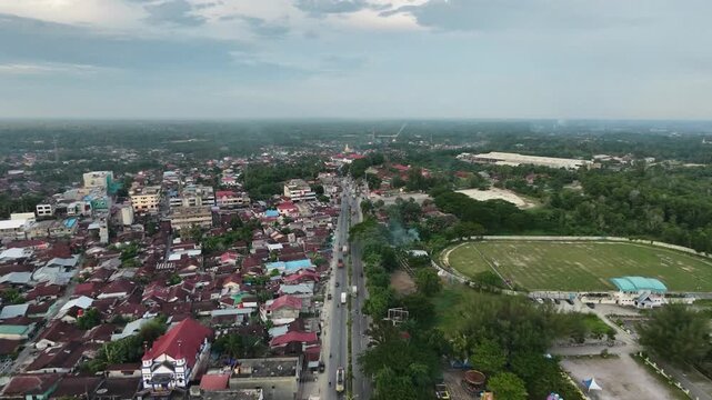 High-angle perspective tracking along a central road dividing a compact community townscape with local buildings and houses. Countryside urban development and lifestyle.