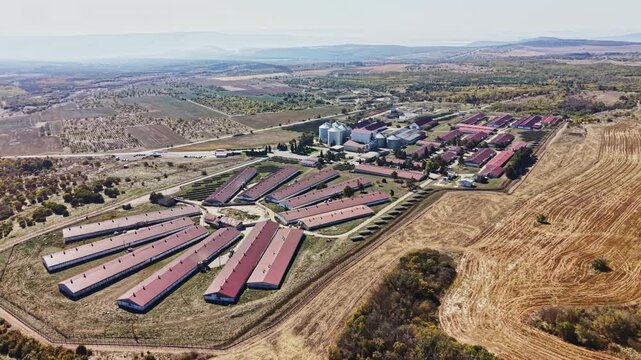 Long farm barns, grain silos, access roads, and livestock enclosures sit beside harvested fields in a rural area, seen from above during daylight.