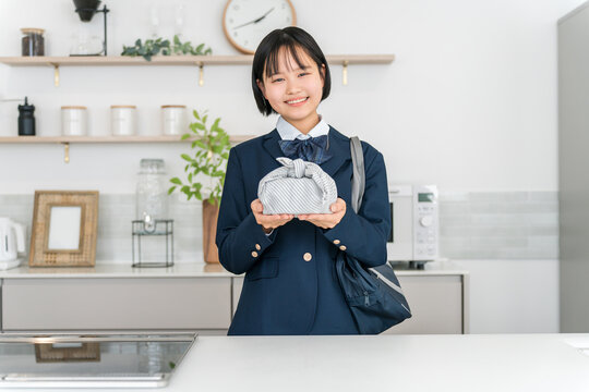 家のキッチンでお弁当を持って笑顔を見せる制服姿の女子高校生