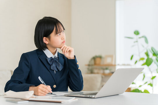 家のリビングでパソコンを使って勉強しながら進路や将来について考える制服姿の女子高校生