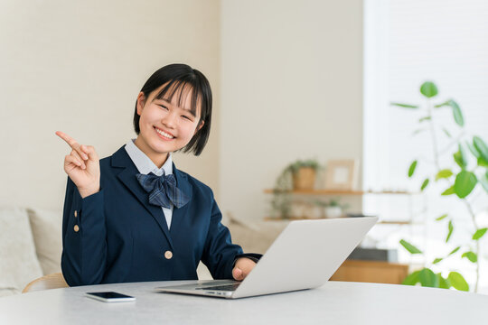 Smiling High School Girl in School Uniform Studying on a Laptop in Her Living Room at Home, Making a Pointing Gesture