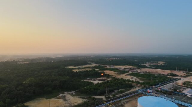 Aerial view of an industrial oil refinery plant with large storage tanks, piping systems, and processing facilities under a glowing sunset sky. Energy, fuel production, and industry concepts