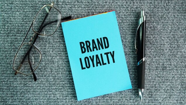 Pen, glasses and paper with the word Brand loyalty is a consumer's consistent preference and commitment to repeatedly buy a specific brand's products or services, even when cheaper 