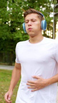 Young man feeling stomach pain in city park during running with strained face and slower pace. Adult boy athlete stopping outdoors after workout with abdominal discomfort heavy breathing and fatigue.