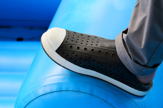 Black perforated shoe resting on blue inflatable surface creates casual outdoor detail with contrast, texture, and playful summer atmosphere for lifestyle imagery