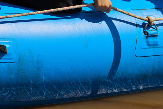 Blue inflatable boat with rope and handle beside calm water, showing bright sunlight, textured surface, and outdoor recreation equipment in close detail