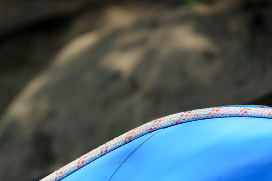 Blue inflatable raft edge with red and white fabric detail against dark rocky background, close up outdoor adventure texture with bright color contrast and shallow focus