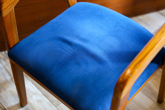 Blue upholstered wooden chair seat with soft fabric texture and polished armrest in warm indoor setting