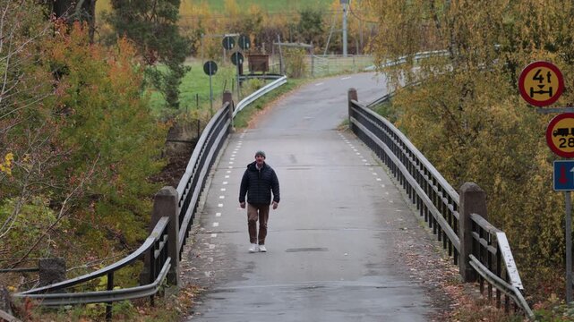 Linkoping, Sweden A man walks over a small bridge surrounded by autumn foliage. 