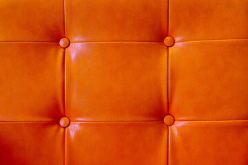 Vivid orange leather upholstery with square tufting and button detail, creating warm luxurious interior texture with geometric symmetry and smooth reflective surface © CoreRock
