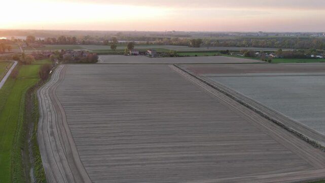 Cultivated fields with parallel soil furrows, curved tractor tracks and scattered farm buildings near Monticelli d'Ongina and Castelvetro Piacentino, Piacenza, Emilia-Romagna, Italy, slow drone flyove