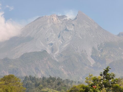 Majestic Mount Merapi Volcano Rising Above Forested Foothills Under A Clouded Blue Sky In Java Indonesia