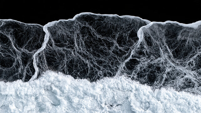 Aerial view of black sand beach, white ocean foam, and dark water forming intricate coastal patterns with dramatic contrast