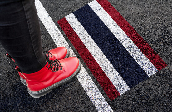 a woman with a boots standing on asphalt next to flag of Thailand and border
