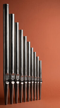 Vertical Array of Metal Pipe Organ Tubes Against Warm Orange Terracotta Wall