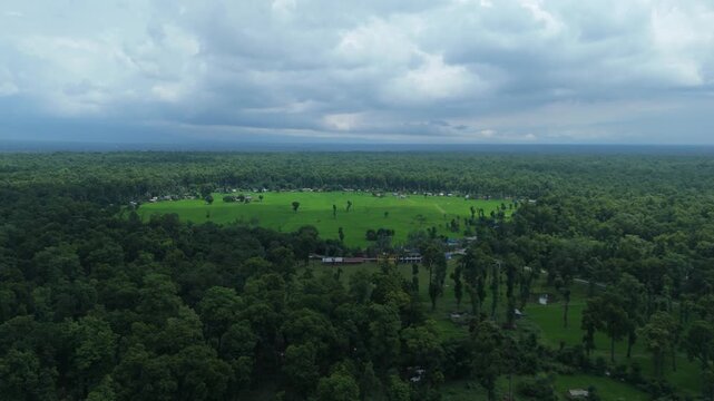 Wide aerial panorama of green agricultural clearing and rural village surrounded by dense forest in Nepal