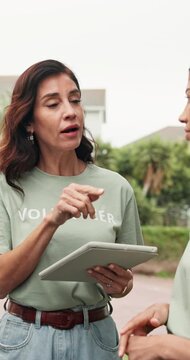 Volunteer, team or woman outdoor with tablet, appointing duty or schedule in charity project. Serious, talking or mature NGO worker with tech, group coordination or task briefing in outreach program.