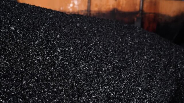 Close-up view of fresh dark asphalt aggregate and gravel mixture loaded inside an industrial hopper during road construction and paving work