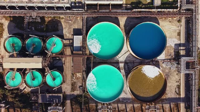 Circular treatment tanks and connected pipes fill a wastewater facility, seen from above in daylight, with water and sediment visible in several basins.