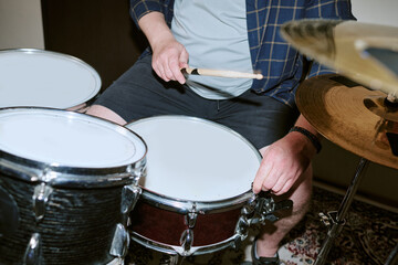 Fototapeta premium Young adult Caucasian male drummer playing acoustic drum set during rehearsal with wooden drumstick, close up. Image suitable for music festival promotion, audio branding, and instrument marketing