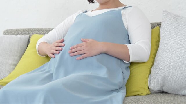ソファに座りお腹をさする女性
