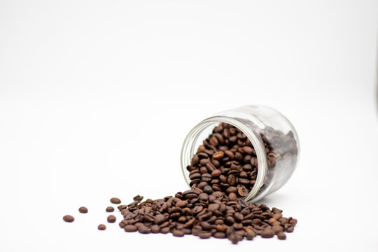 Coffee beans spilling from a glass jar on a white background   