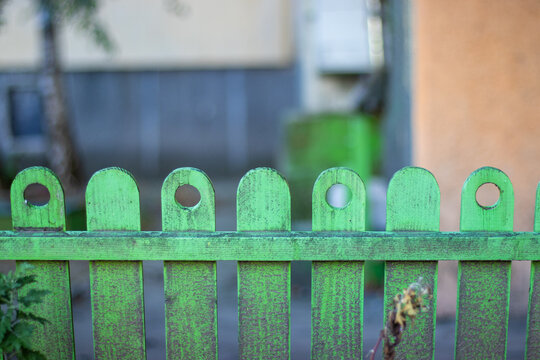 Green wooden picket fence with circular holes and weathered texture   
