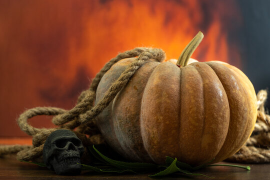 Halloween still life with rustic pumpkin, hemp rope, and a skull against a fiery background   