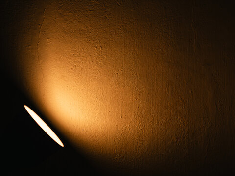 Warm golden spotlight glowing on a dark textured plaster wall with rough surface and a thin crack, moody low-key light and shadow background with copy space
