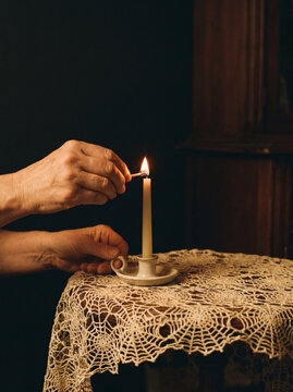 Hands lighting a taper candle on a lace covered table in a dark room
